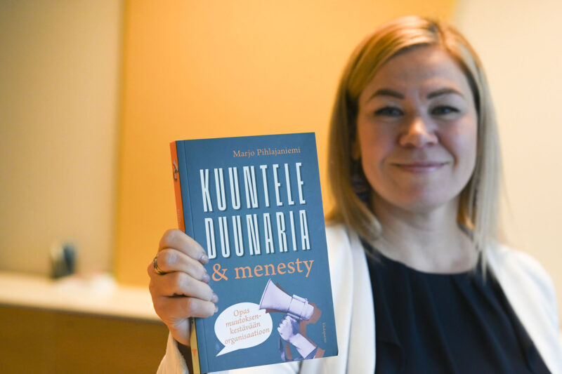 Marjo Pihlajaniemi kädessä kirja Kuuntele duunaria ja menesty.
